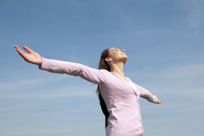 Low angle view of mid adult woman with arms outstretched standing against blue sky