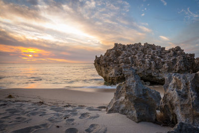 Rock on beach against sky during sunset