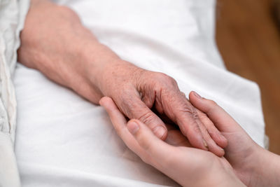 Woman holding grandmother's hand on bed