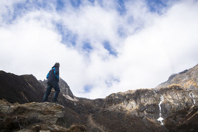 Low angle view of person standing on rock against sky