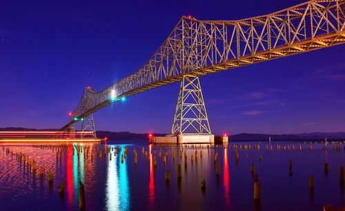 Illuminated bridge over river against sky at night