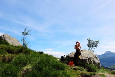 Woman sitting on rock against sky