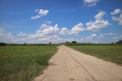 Empty road amidst field against sky