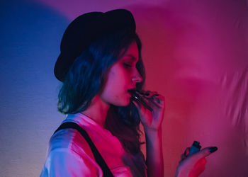 Portrait of young woman looking away against pink wall