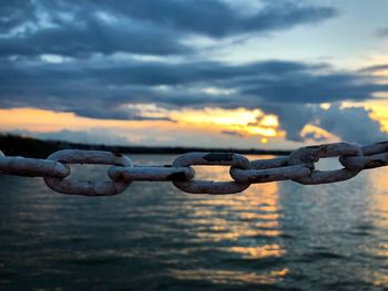 Close-up of chain on water against sky during sunset