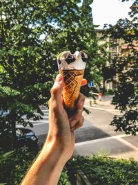 Woman holding ice cream cone against trees