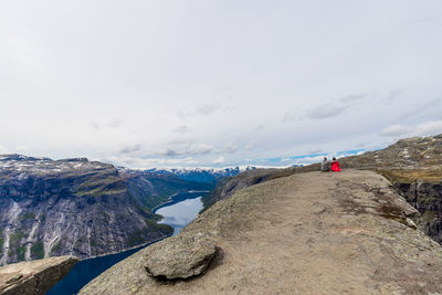 Man and woman sharing a hug sitting on edge of trolltunga rock in western norway.