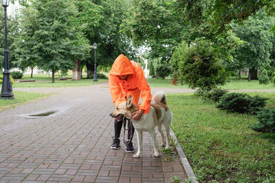 Rainy weather. young woman in orange raincoat walking with her dog in a summer park