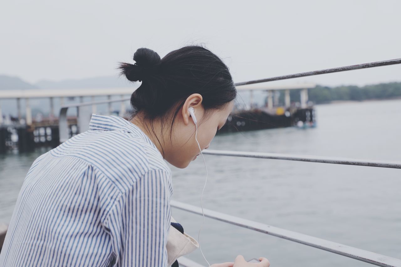 one person, real people, water, lifestyles, leisure activity, focus on foreground, young women, transportation, standing, casual clothing, young adult, architecture, nautical vessel, railing, hair, adult, nature, sky, hairstyle, outdoors