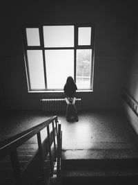 Rear view of woman standing by window at home