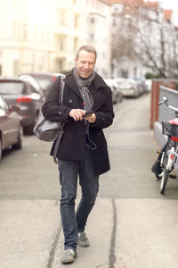 Smiling man listening music through headphones while walking on footpath
