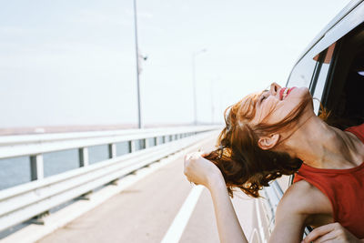 Woman sitting on railing against sky