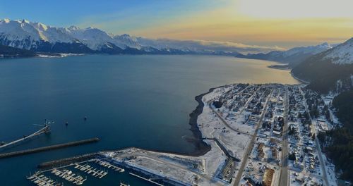 Aerial view of city by sea against sky during sunset