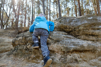 Rear view of girl climbing rock formation in forest