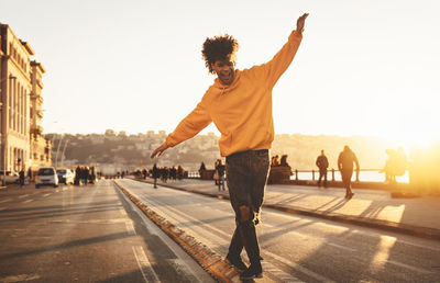 Full length of man walking on street in city against clear sky at sunset