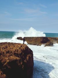 Rear view of man standing on rock by sea against sky