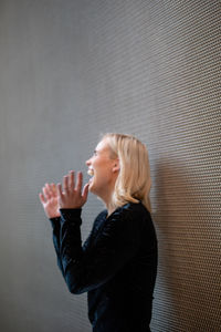 Side view of smiling woman standing by wall