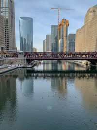 Bridge over river by buildings against sky in city