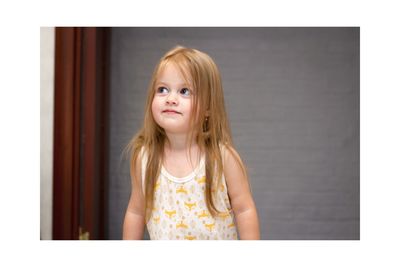 Portrait of little girl standing against wall