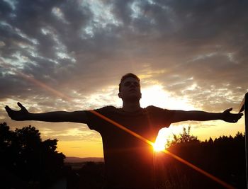 Silhouette man with arms outstretched against sky during sunset