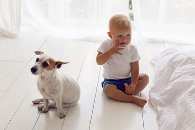 Child in a white t-shirt and shorts sit at home by the window with dog