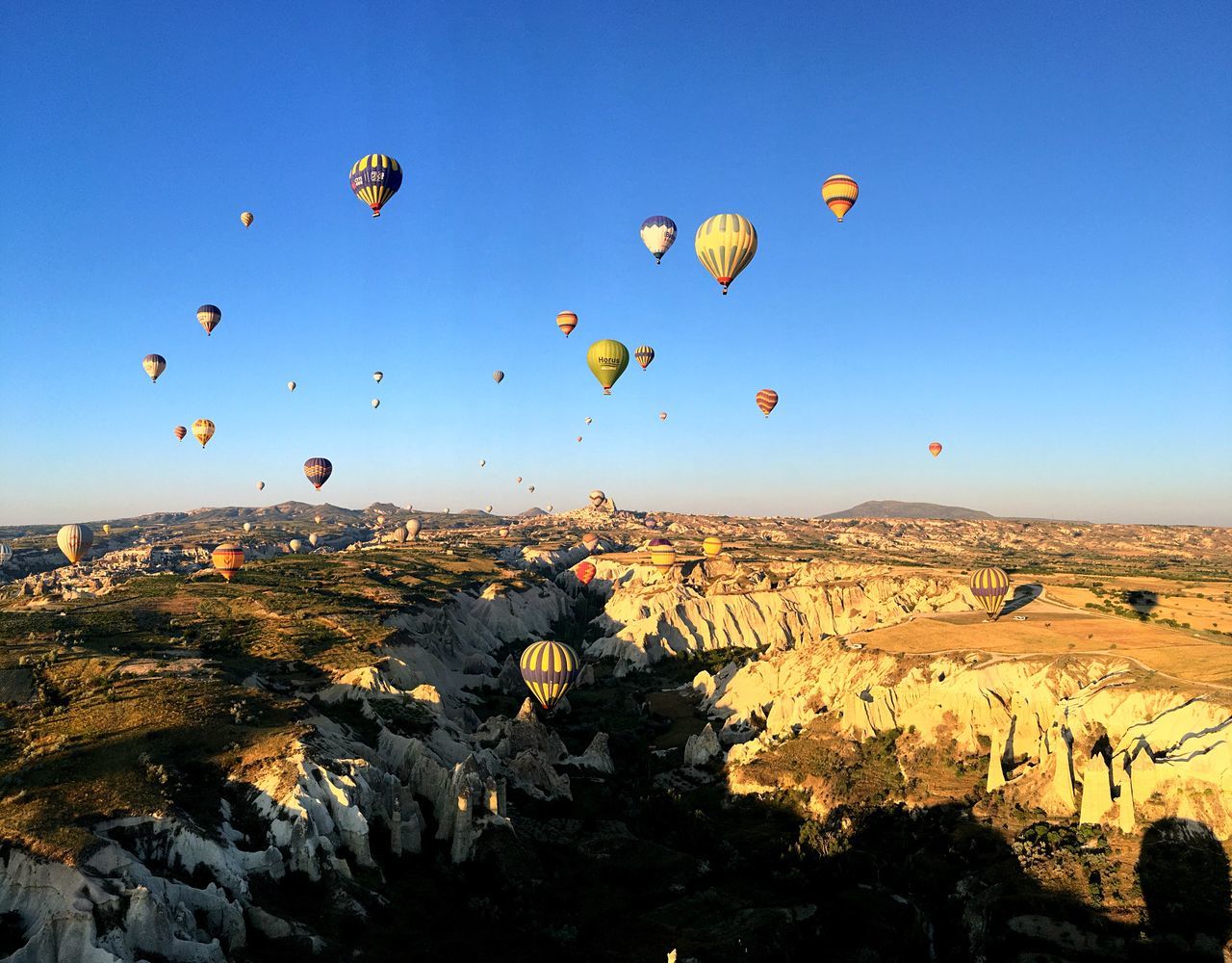 hot air balloon, rock formation, mid-air, landscape, rock - object, rock hoodoo, nature, ballooning festival, scenics, blue, flying, outdoors, beauty in nature, clear sky, tranquil scene, tranquility, no people, mountain, sky, day, multi colored