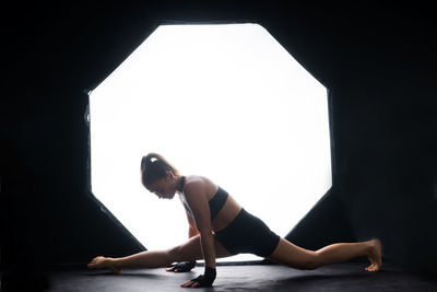 Side view of woman exercising against black background