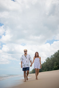 Man and woman walking at beach against sky