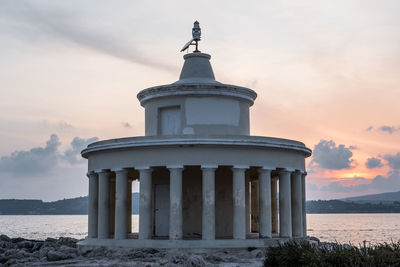 Built structure on beach by sea against sky during sunset