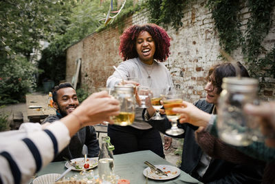 Woman with curly hair toasting drinks with friends during social gathering in back yard