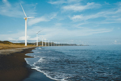 Wind turbines at beach against sky