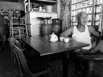 Senior man sitting on chair in kitchen at home