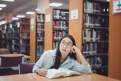 Bored young woman sitting with book at library
