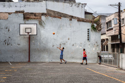 Full length of friends playing basketball against buildings
