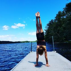 Rear view of gymnast practicing handstand on pier against lake