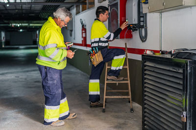 Side view of group of professional male technicians with electric tools repairing and checking equipment while working in building