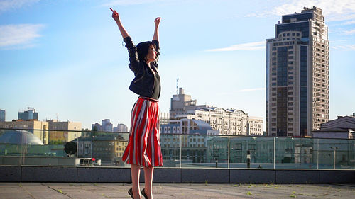 Happy woman wearing striped skirt and jacket on footpath in city