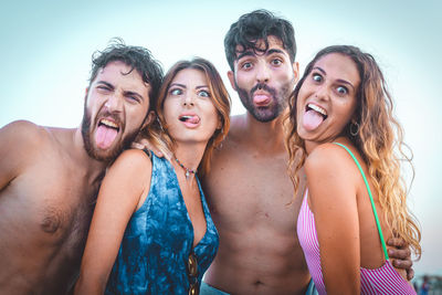 Portrait of cheerful couples sticking out tongue against sky