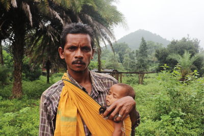A tribal man carrying his child in a sling in a natural backdrop
