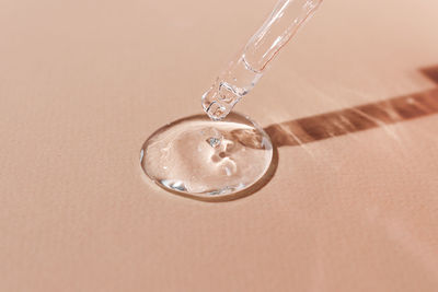 A sample of transparent hyaluronic acid on a beige background flows down from a glass pipette.