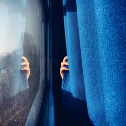 Close-up of hand holding curtain against window