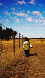 Rear view of man standing on field against sky