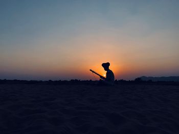 Silhouette man playing string music against sky during sunset