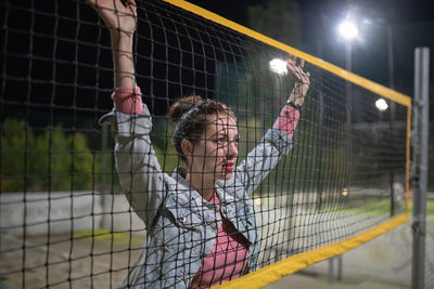 Woman leaning on net at night