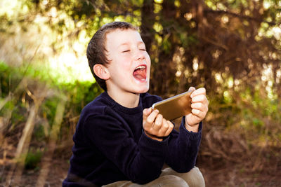 Boy holding mobile phone while sitting outdoors