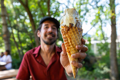Man holding ice cream cone against trees