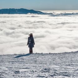 Rear view of woman standing on snow covered cliff against cloudscape