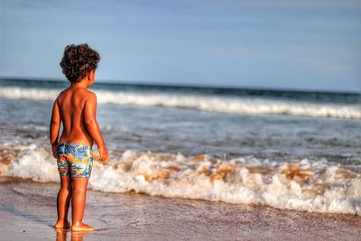 Rear view full length of shirtless boy standing on shore at beach