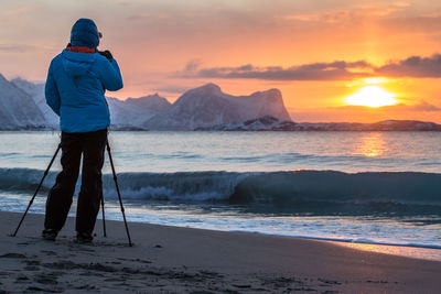 Man photographing sea against sky during sunset