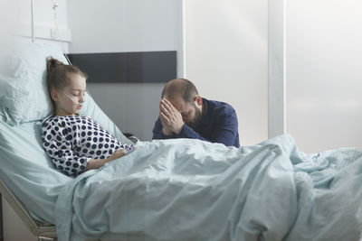 Worried man sitting by daughter's bed in hospital ward